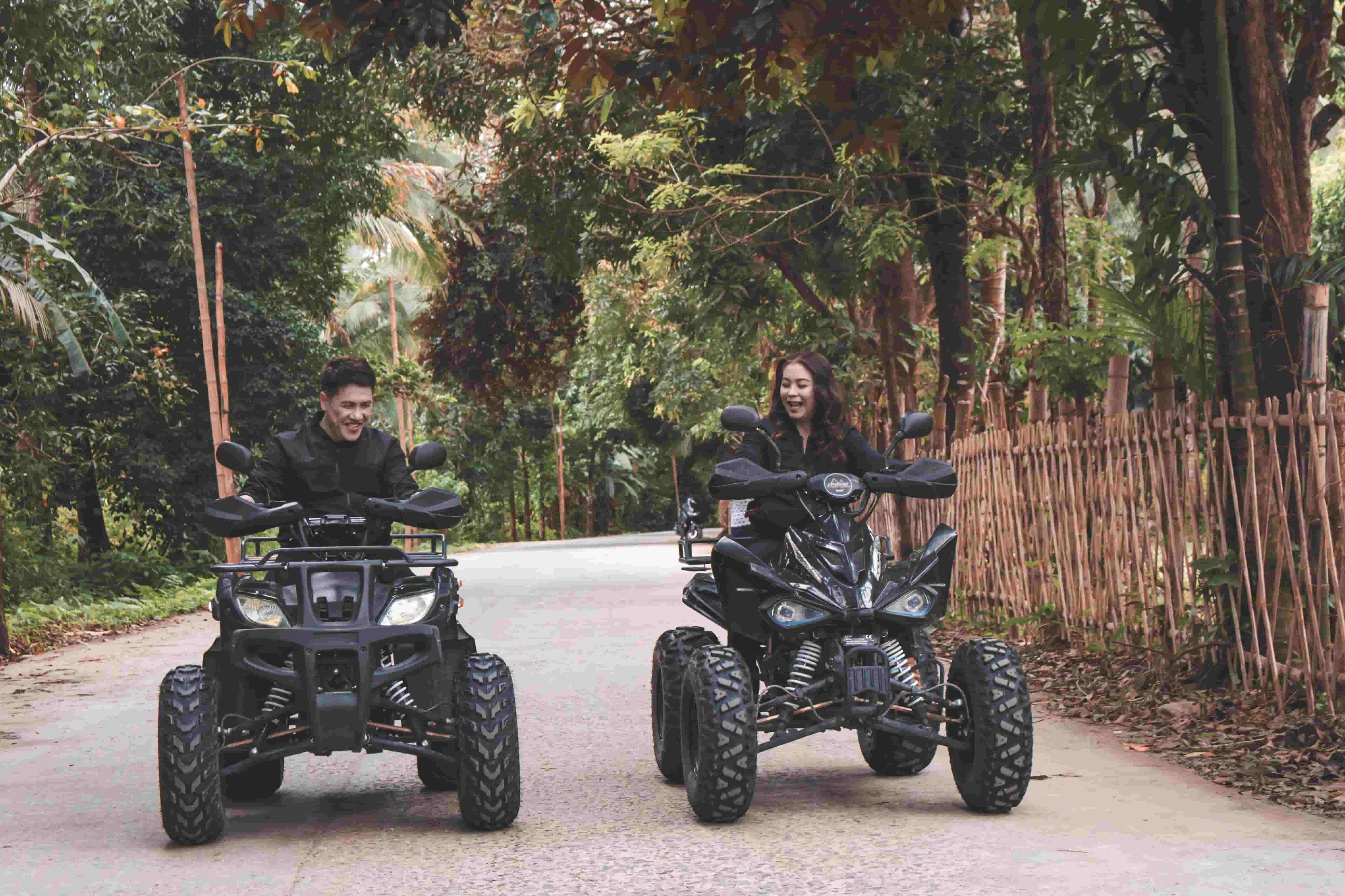 Two riders on ATVs riding along a wooded path