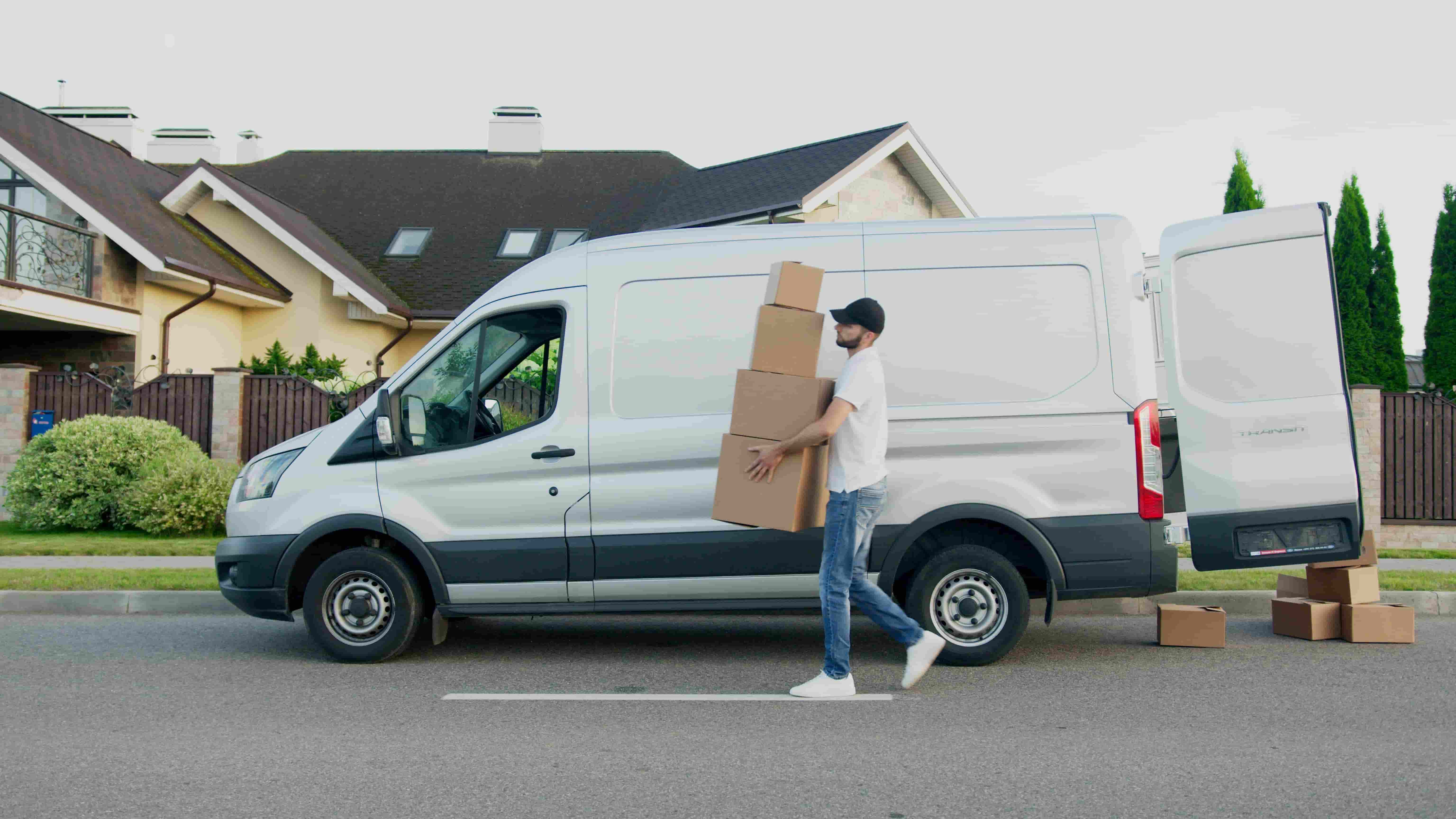 Delivery worker carrying stacked boxes past a white cargo van parked on a residential street