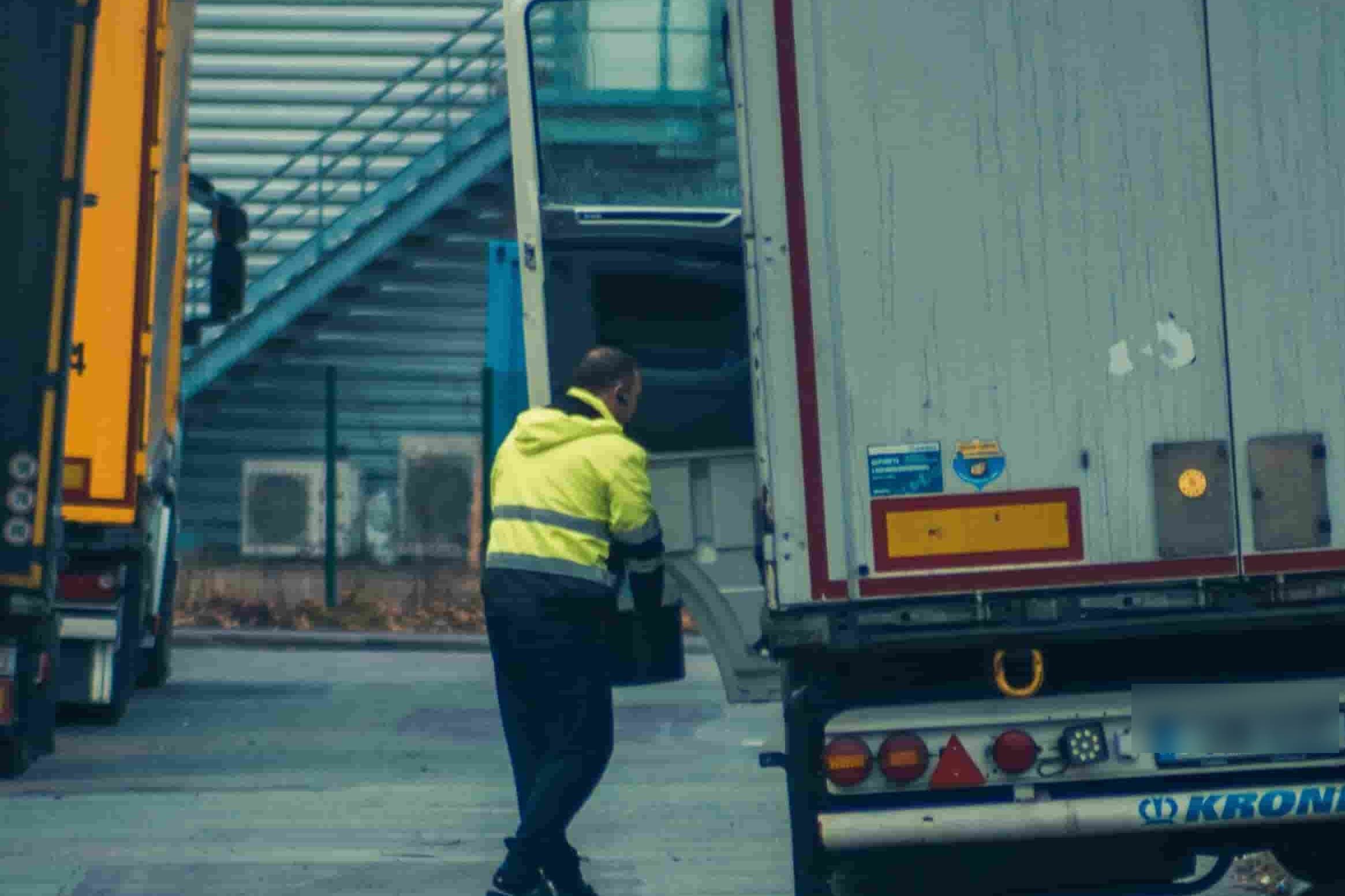 Truck driver in a high-visibility jacket stepping up to the open cab door of a semi truck