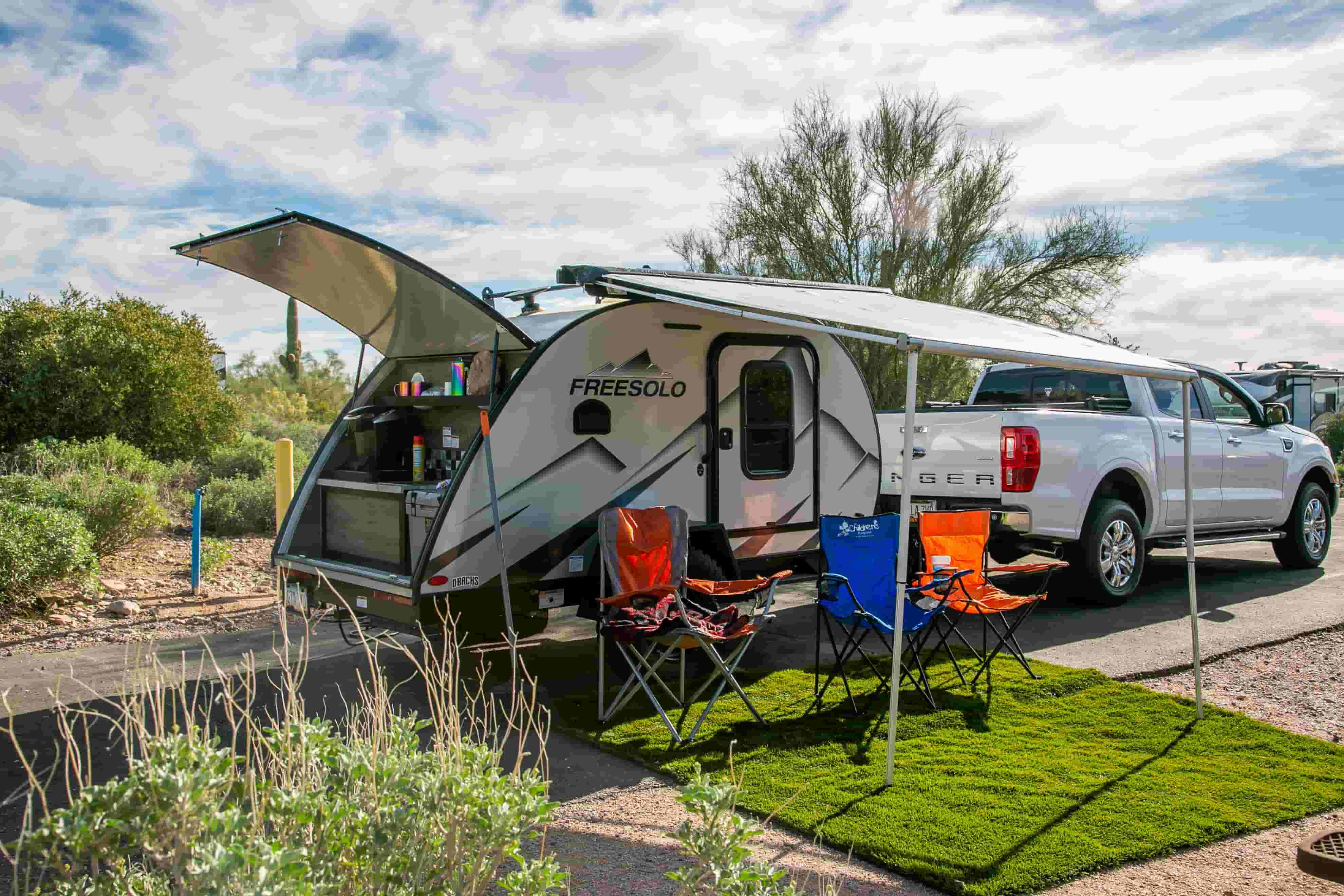 Teardrop travel trailer with an open galley and awning, hitched to a pickup at a desert campground