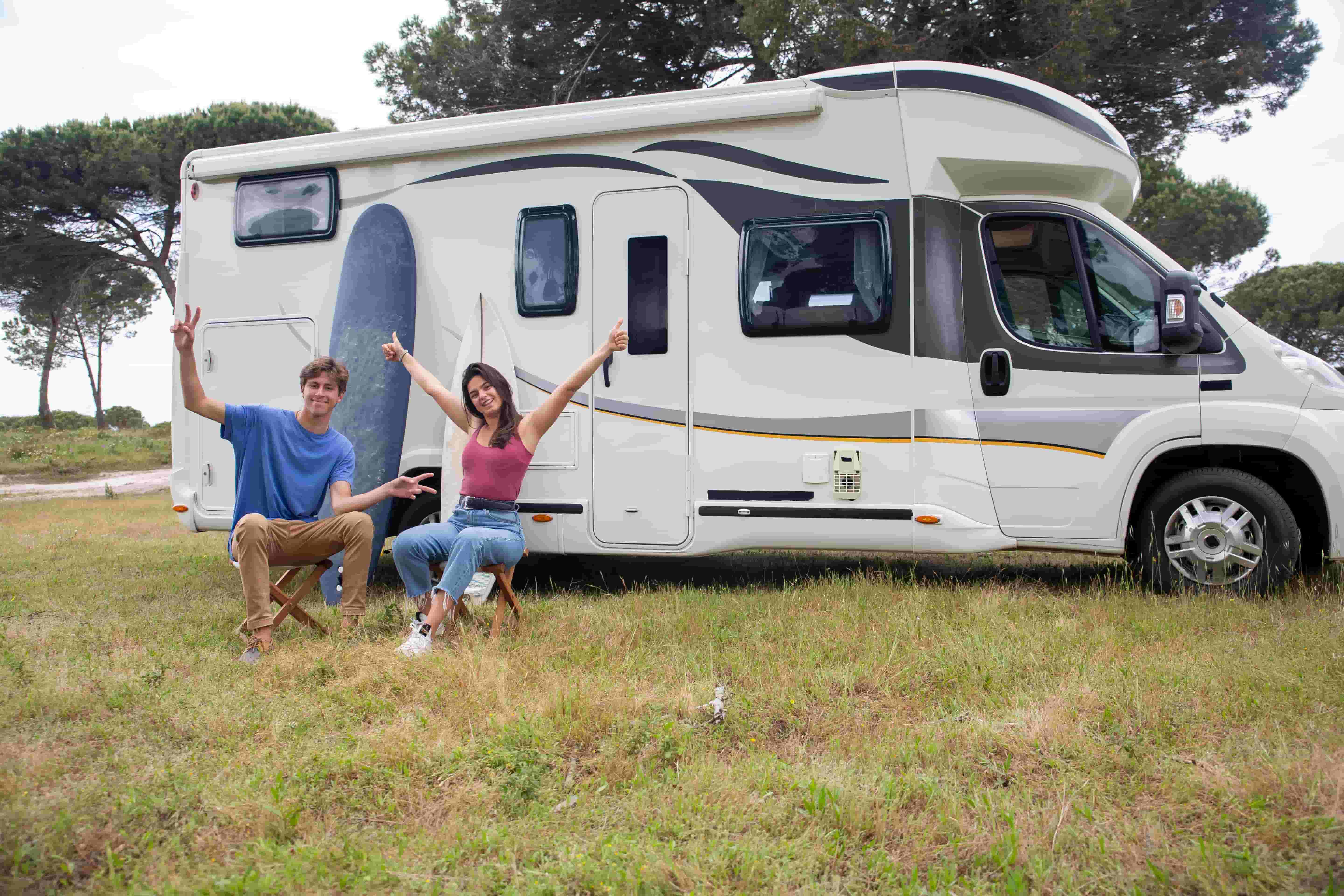 Couple relaxing beside a Class C motorhome at a grassy campsite