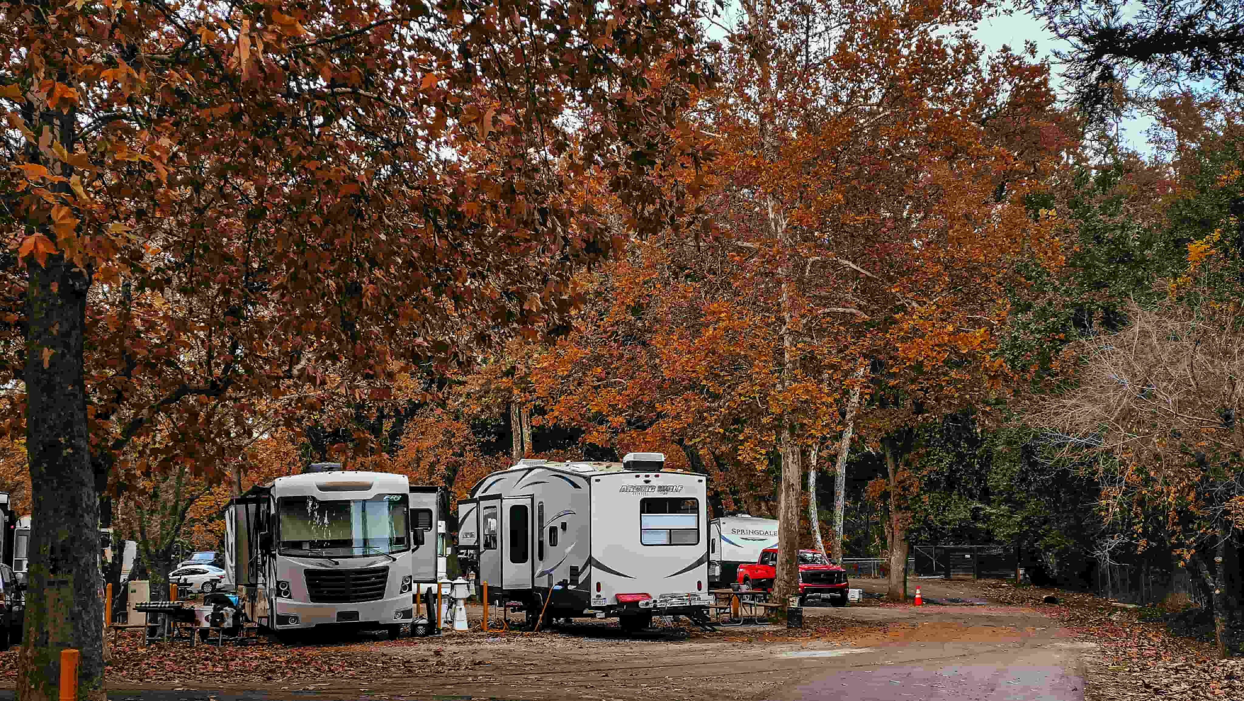 Class A motorhome and travel trailer parked at a campground in fall