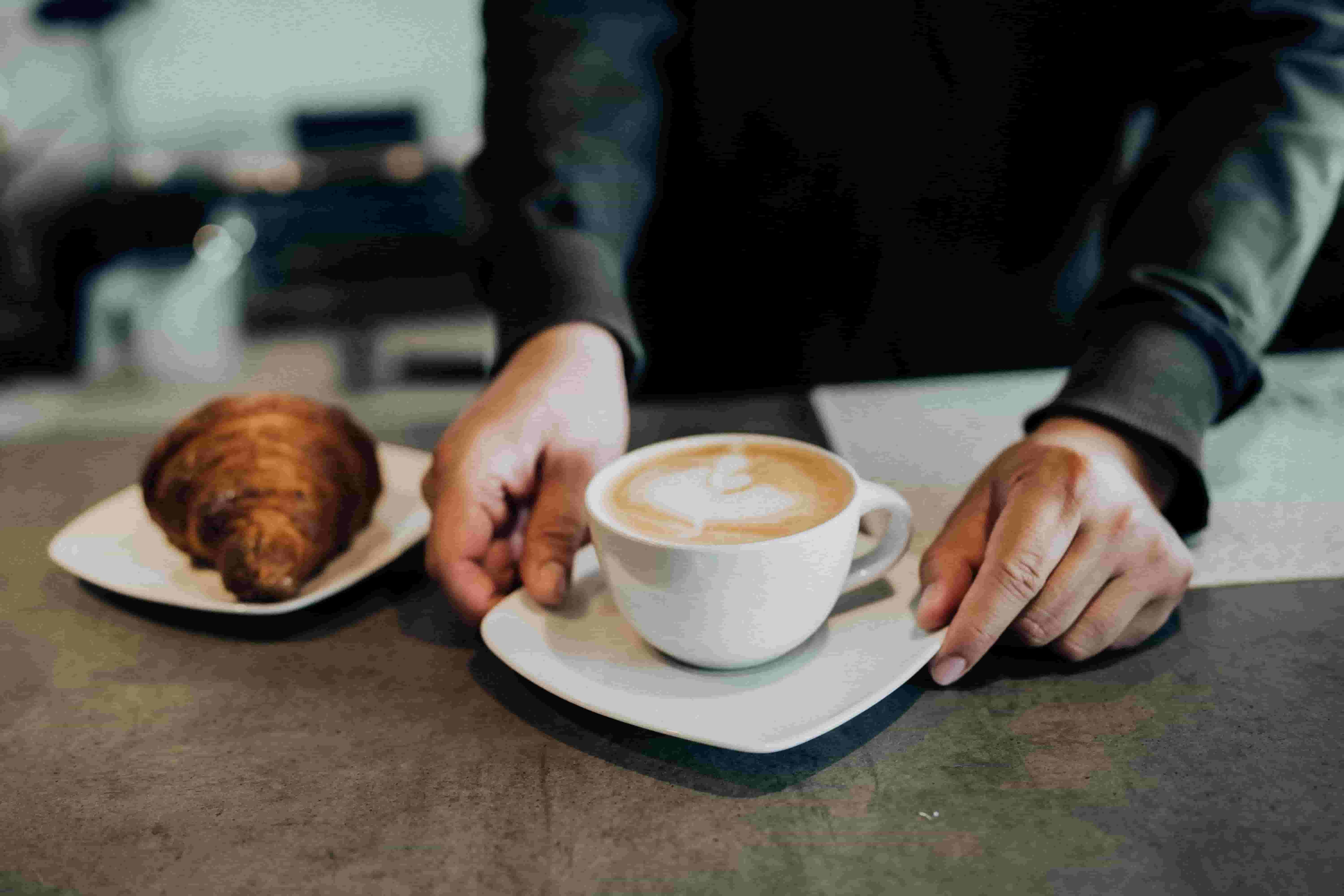 Barista handing a customer a cappuccino and pastry across the counter of a coffee shop