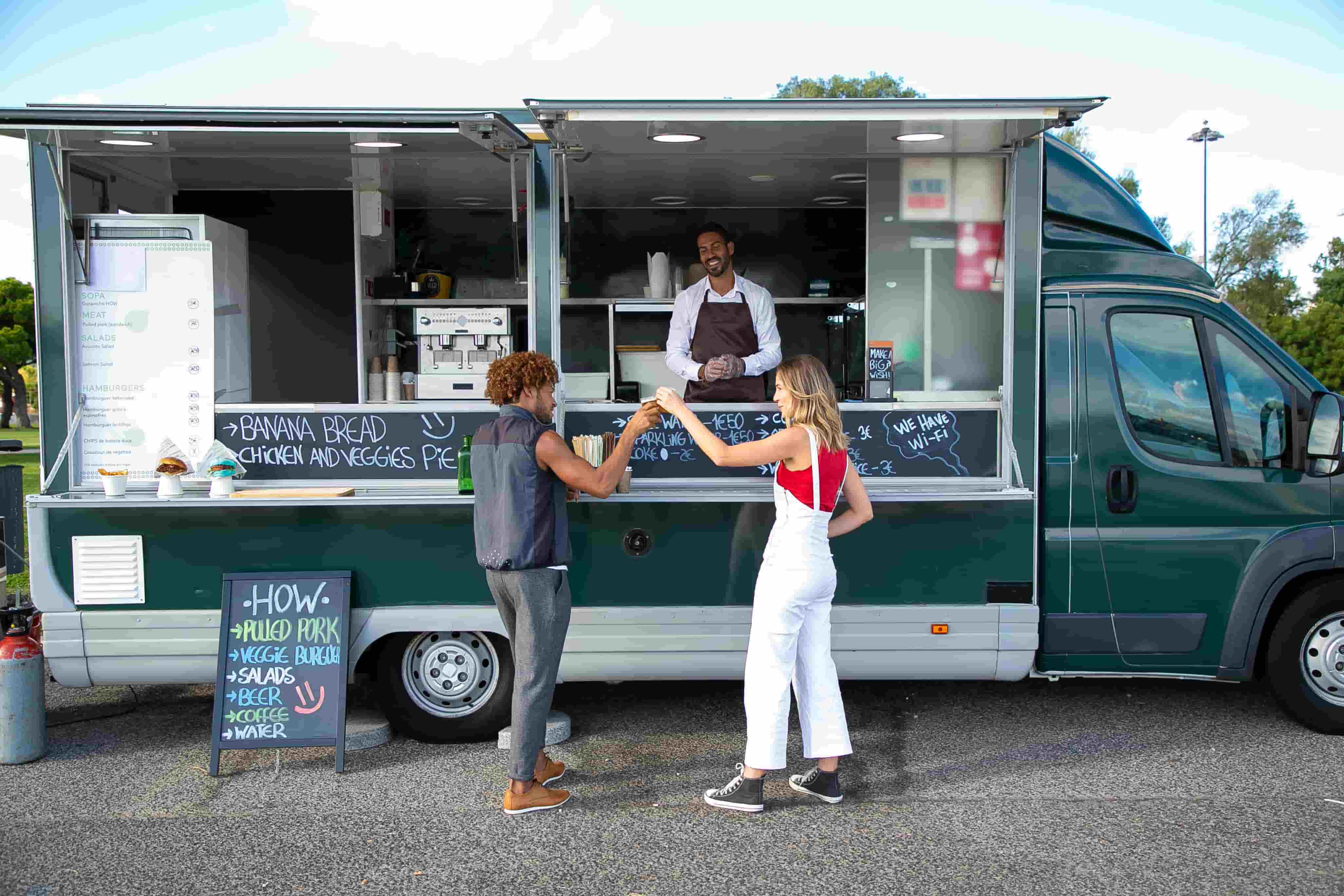 Food truck owner serving customers at the service window beside chalkboard menus