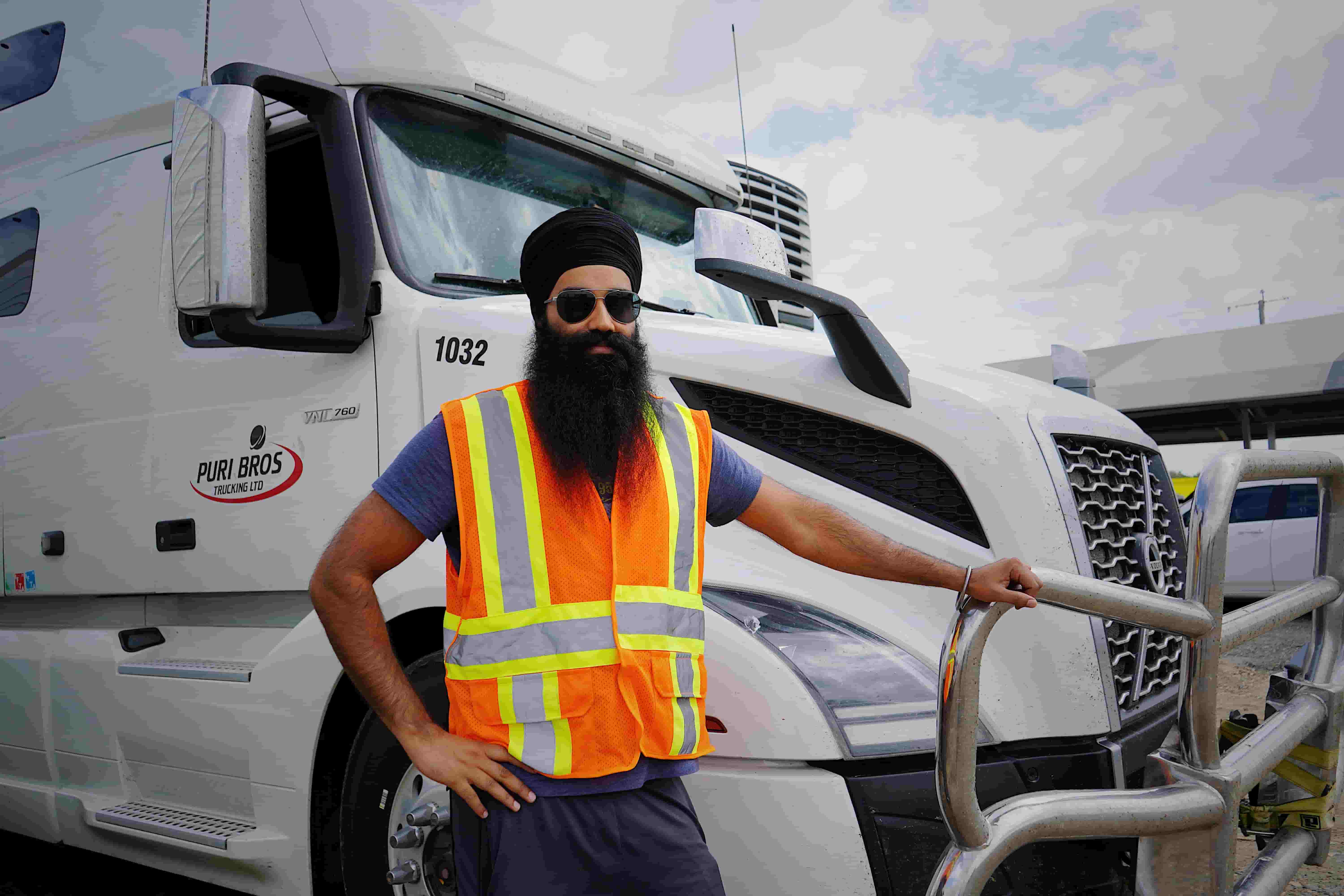 Owner-operator in a safety vest standing beside a Volvo semi truck