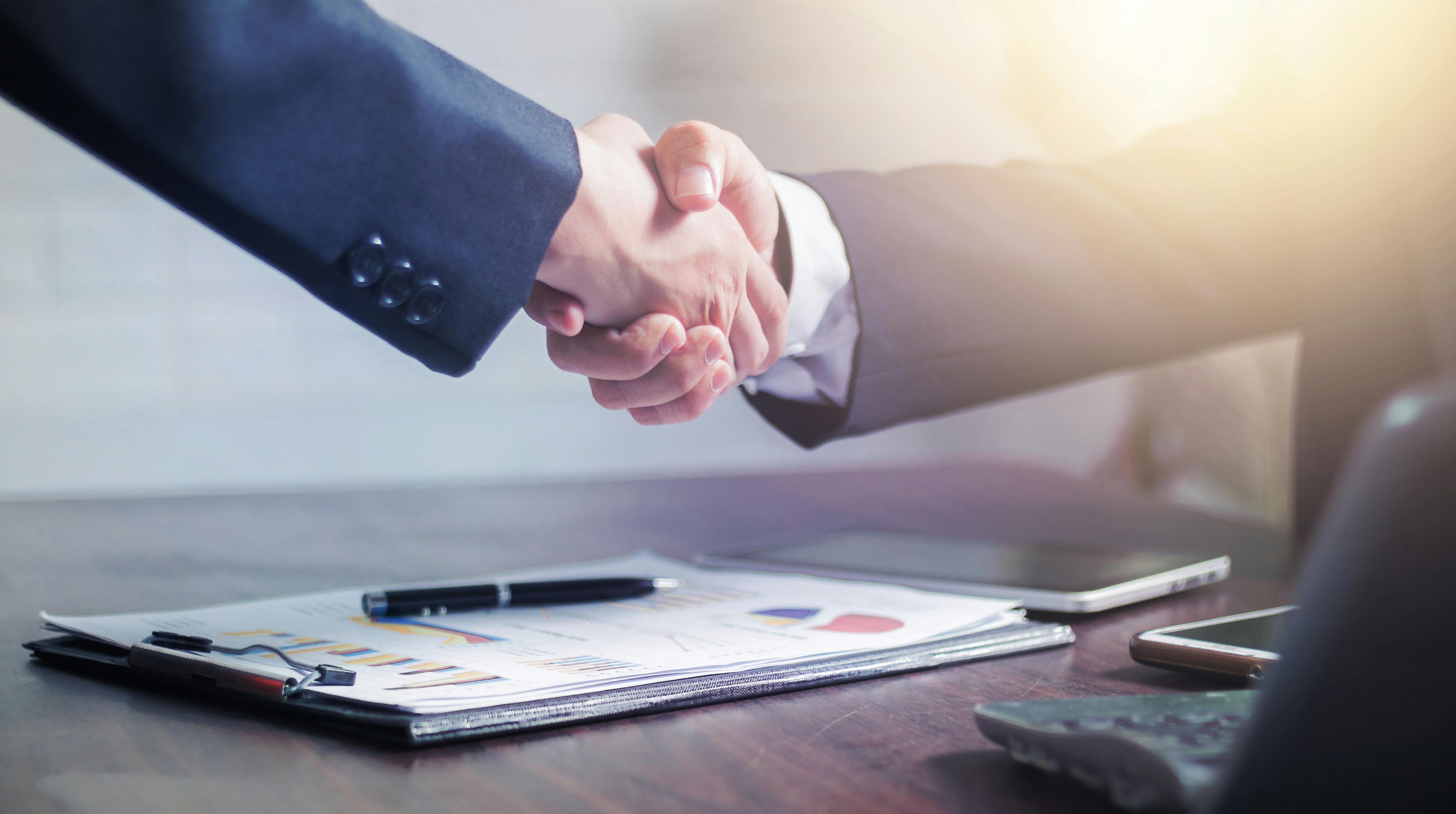 Two people shaking hands over a clipboard of business documents