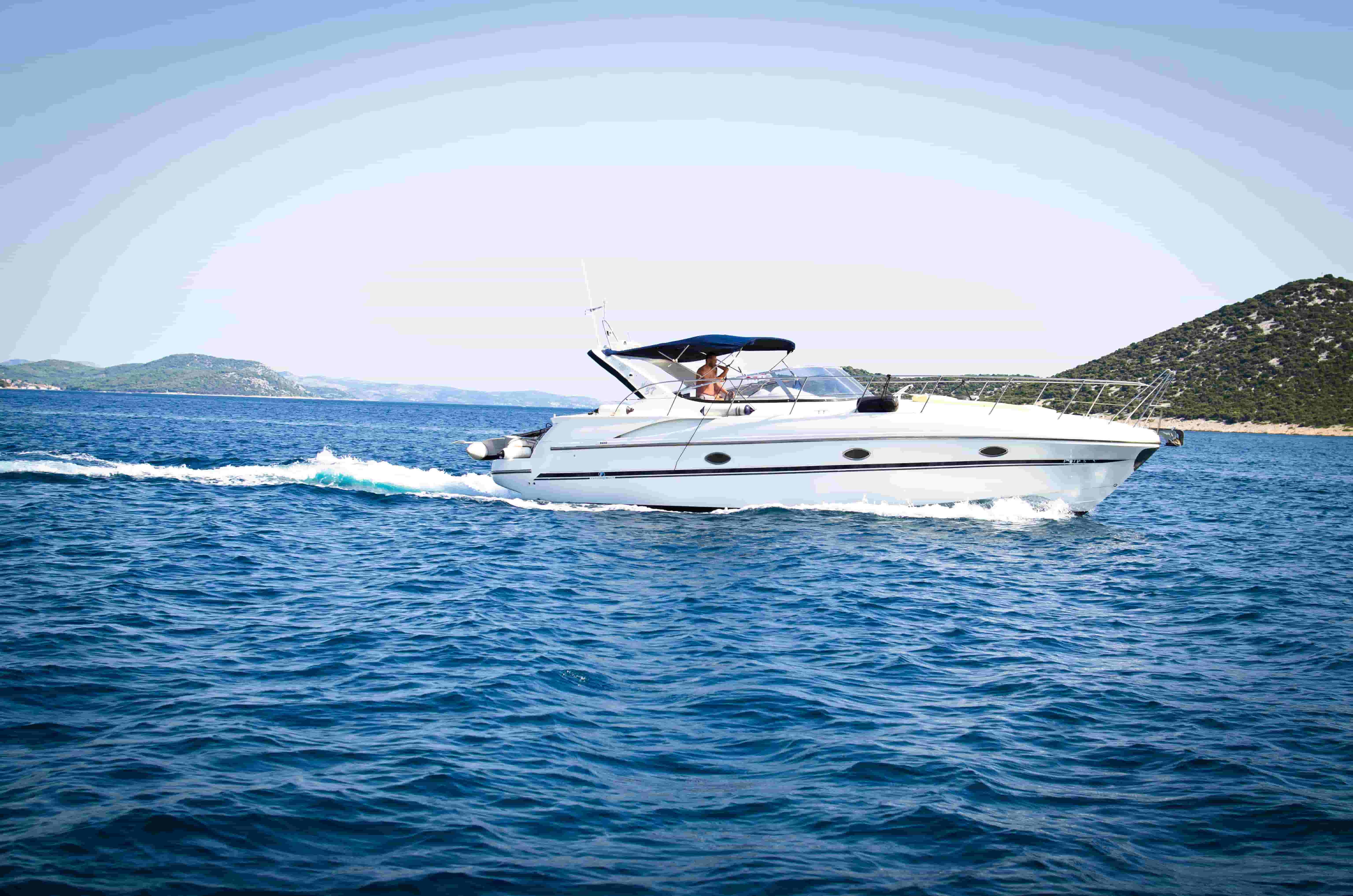 White express cruiser with a navy bimini top running across open blue water past a wooded shoreline